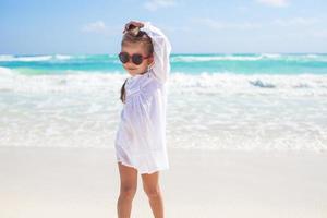 Schönes kleines Mädchen, das sich an einem sonnigen Tag an einem exotischen weißen Strand amüsiert foto