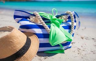 Streifentasche, Strohhut, Sonnencreme und Frisbee am weißen tropischen Sandstrand foto
