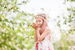 kleines schönes Mädchen, das Geruch in einem blühenden Frühlingsapfelgarten genießt foto