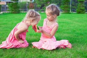 Kleine entzückende Mädchen, die im Sommer eine reife saftige Wassermelone essen foto