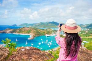 junge touristische frau, die foto des englischen hafens von shirley heights, antigua, paradiesbucht auf tropischer insel in der karibik macht