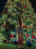 junges Mädchen auf dem Hintergrund des Weihnachtsbaums in Miami. schöner weihnachtsbaum in der beliebten gegend am weihnachtsabend und lichter foto