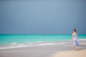 schönes kleines Mädchen im Kleid am Strand, das Spaß hat. foto