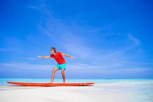 glücklicher junger mann, der surfposition auf surfbrett übt foto