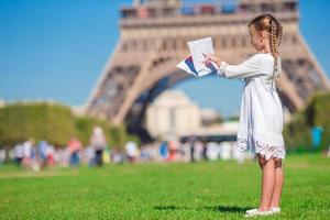 entzückendes kleines mädchen mit karte von paris hintergrund der eiffelturm foto