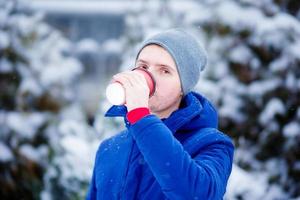 junger kaukasischer mann, der kaffee am gefrorenen wintertag draußen trinkt foto