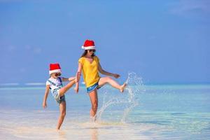 kleines mädchen und junge mutter in weihnachtsmützen während des strandurlaubs foto