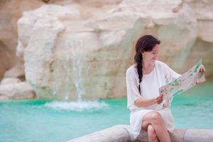 schöne frau, die touristischen stadtplan nahe trevi-brunnen, rom, italien betrachtet. glückliches mädchen genießt italienischen urlaub in europa. foto