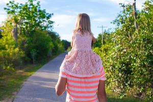kleines Mädchen, das auf ihrem Vater reitet und im Garten spazieren geht foto