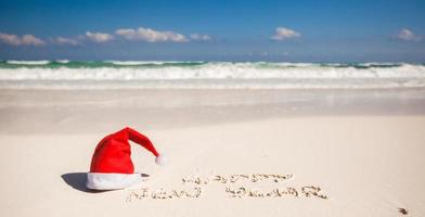 Frohes neues Jahr geschrieben in den Sand und die Weihnachtsmütze am weißen Sandstrand foto