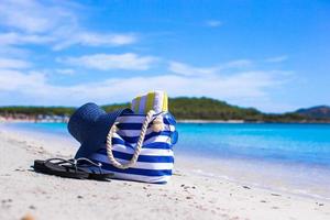 Blaue Tasche, Strohhut, Flip-Flops und Handtuch am weißen tropischen Strand foto