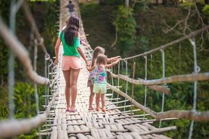 Rückansicht kleiner Mädchen und junger Frauen, die auf einer Hängebrücke über den Fluss Loboc, Philippinen, gehen foto