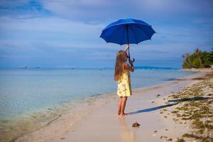 kleines Mädchen mit einem Regenschirm in den Händen am weißen Sandstrand foto