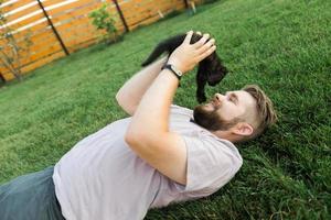 mann mit kleinem kätzchen, das auf gras liegt und spielt - freundschaftsliebestiere und haustierbesitzerkonzept foto