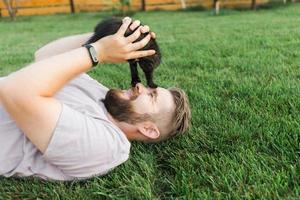 mann mit kleinem kätzchen, das auf gras liegt und spielt - freundschaftsliebestiere und haustierbesitzerkonzept foto