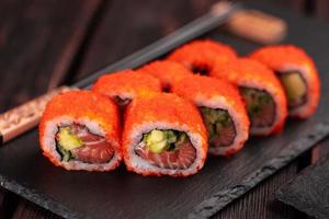 kalifornische sushi-rolle mit lachs, avocado, gurke und tobiko-kaviar, serviert auf tafelnahaufnahme - japanisches essen foto