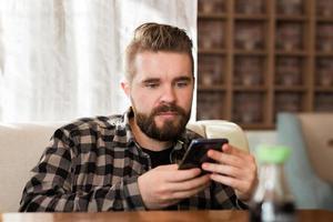Lächelnder Mann mit Smartphone im modernen Café, er chattet Online-Messaging auf dem Handy. Konzept für soziale Netzwerke und Millennials foto