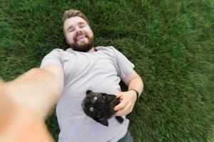 mann mit kleinem kätzchen, das auf gras liegt und spielt - freundschaftsliebestiere und haustierbesitzerkonzept foto