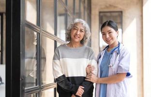 junge Pflegekraft hilft Seniorin beim Gehen. krankenschwester unterstützt ihre alte patientin im pflegeheim. Seniorin mit Spazierstock, der zu Hause von einer Krankenschwester geholfen wird. foto