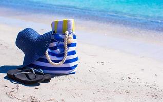 Strohhut, Tasche und Handtuch am weißen tropischen Strand foto