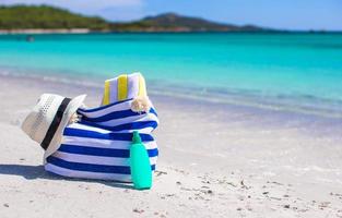 Streifentasche, Strohhut, Sonnencreme und Handtuch am Strand foto