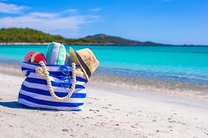 blaue Tasche, Strohhut, Flip Flops und Handtuch am weißen Strand foto