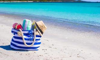 blaue Tasche, Strohhut, Flip Flops und Handtuch am weißen Strand foto