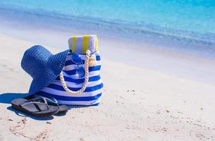 Strohhut, Tasche und Handtuch am weißen tropischen Strand foto