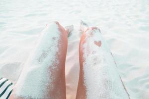 Frauenfüße am weißen Sandstrand im seichten Wasser foto