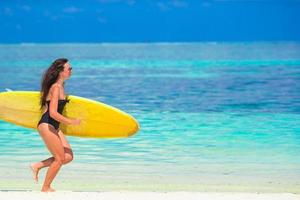 glückliche formschöne surffrau am weißen strand mit gelbem surfbrett foto