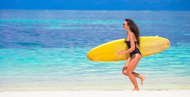 glückliche formschöne surffrau am weißen strand mit gelbem surfbrett foto