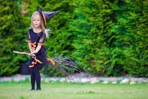 Kleines entzückendes Mädchen im Halloween-Kostüm, das sich auf dem Besen amüsiert. Süßes oder Saures. foto