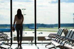 junge Frau am Fenster in einer Flughafenlounge, die auf Flugflugzeuge wartet foto