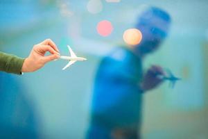 Nahaufnahmehand, die ein Flugzeugmodellspielzeug am großen Fenster des Flughafenhintergrundes hält foto