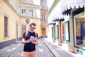 mann tourist mit stadtplan und rucksack in der europastraße. kaukasischer junge, der mit karte der europäischen stadt schaut. foto