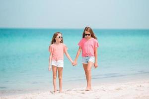 Kleine Mädchen, die sich am tropischen Strand amüsieren und zusammen im seichten Wasser spielen foto