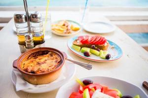 Traditionelles Mittagessen mit Musaka und köstlichem frischem griechischen Salat, serviert zum Mittagessen im Restaurant im Freien mit herrlichem Blick auf das Meer und den Hafen foto