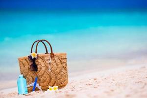 strandkonzept - strohbeutel, hut, sonnenbrille und sonnencremeflasche am weißen strand foto