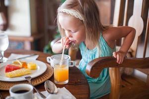 entzückendes kleines mädchen, das frühstückt und fruchtcocktail trinkt foto