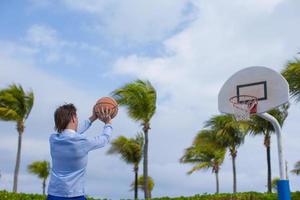 junger Mann, der draußen im exotischen Resort Basketball spielt foto