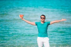 glücklicher mann, der spaß am strand hat und wassermelone isst foto