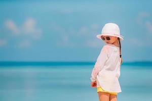 Entzückendes kleines Mädchen mit Hut am Strand während der Sommerferien foto