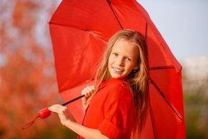 glückliches Kindermädchen lacht unter rotem Regenschirm foto