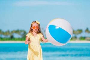 Kleines entzückendes Mädchen, das am Strand mit Ball spielt foto