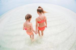 Entzückende kleine Mädchen haben gemeinsam Spaß am weißen tropischen Strand foto