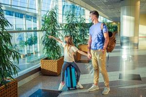 Papa und kleines Mädchen mit medizinischen Masken am Flughafen. Schutz vor Coronavirus und Grip foto