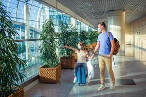 Papa und kleines Mädchen mit medizinischen Masken am Flughafen. Schutz vor Coronavirus und Grip foto