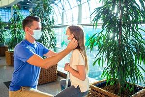 Papa und kleines Mädchen mit medizinischen Masken am Flughafen. Schutz vor Coronavirus und Grip foto