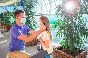 Papa und kleines Mädchen mit medizinischen Masken am Flughafen. Schutz vor Coronavirus und Grip foto