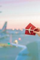 Nahaufnahmehand, die ein Flugzeugmodellspielzeug und Pässe am großen Fenster des Flughafenhintergrundes hält foto